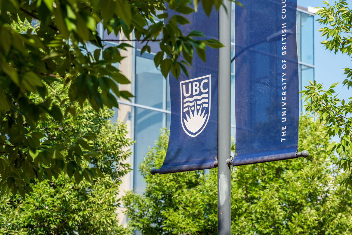 Dark blue UBC banner against glass building and green foliage.