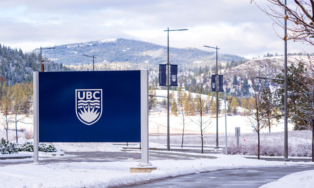 UBC sign at UBC Okanagan, with snow on the ground and snowy hills in the background.