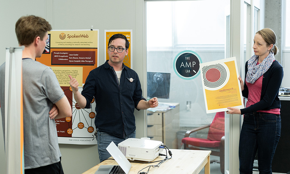 Three people work together in a classroom to create a research display