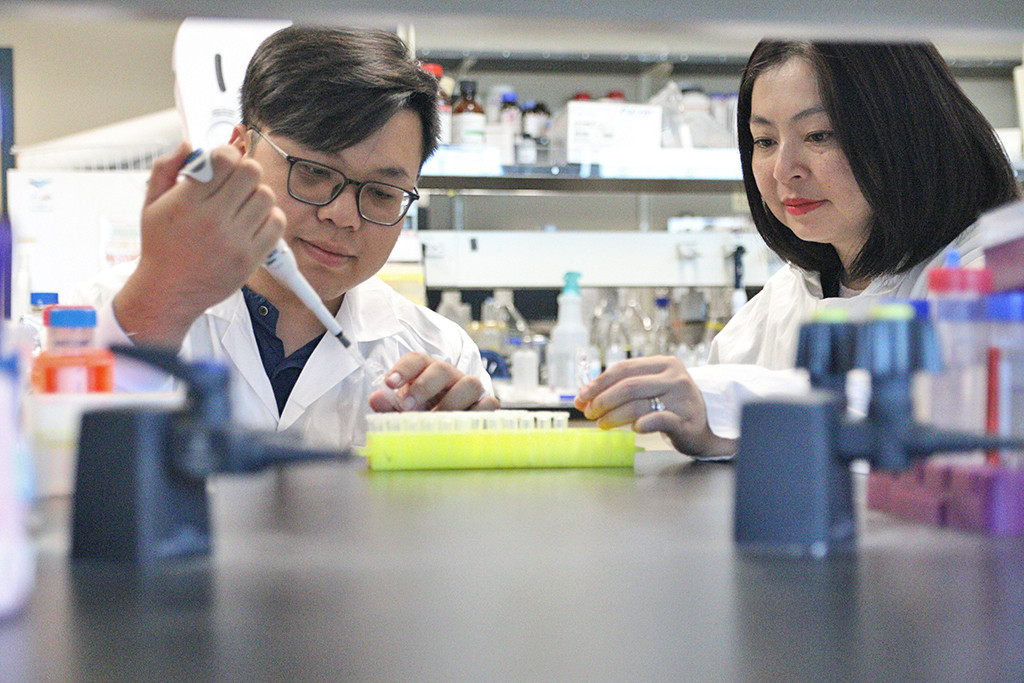 Two researchers in a laboratory setting: doctoral student Tuan-Anh Nguyen on the left and Dr. Thu-Thuy Dang examining plant samples. They are conducting research on how tropical trees produce mitraphylline, a rare compound with potential anti-cancer properties at UBC Okanagan.